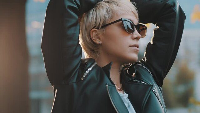 Young woman with bright hair and sunglasses posing in park with hands over the head. Close up. High quality 4k footage