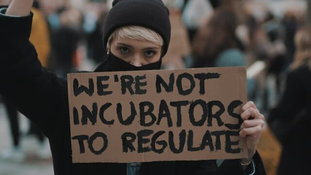Womens march. Young woman with face mask protesting with banner sign - We are not incubators to regulate. protest against strict abortion laws. High quality 4k footage