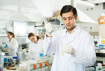 Fototapeta premium Intelligent student performing experiments in university laboratory, using mechanical lab pipette for mixing chemicals..