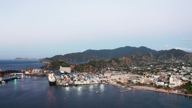 Drone shot of harbour of Santa Marta Colombia around sunset viewing the bay, ships, industry, tourist hotels, houses, beach and mountains 4k