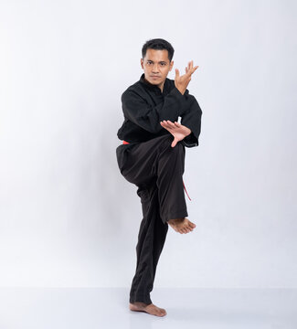 Asian boy with defensive pose raises one leg while wearing a pencak silat uniform on a white background