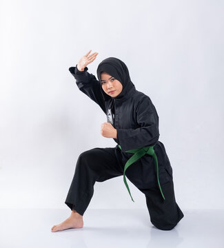 Asian women in headscarves wear pencak silat uniforms with squat green belts while performing defensive movements on the isolated background