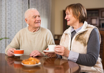 Fototapeta na wymiar Cheerful elderly man and woman enjoying conversation over cup of coffee at home..
