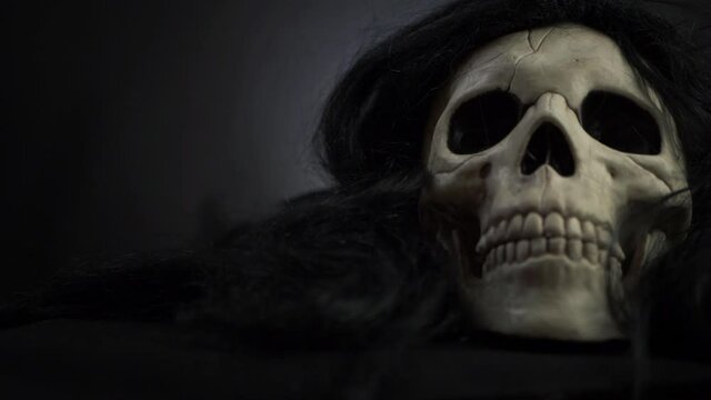 Creepy skull with black hair on dark background medium panning shot