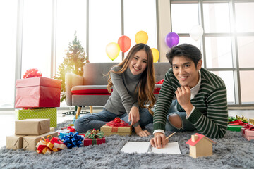 Season greeting. A couple writing in a notebook while celebrates the winter holiday near the Christmas tree. Merry Christmas and Happy New Year. Real estate investing, property business concepts. 