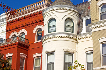 A row of historic townhouses in Washington DC, USA. Brick houses with colorful ornate facades in autumn under blue sky.