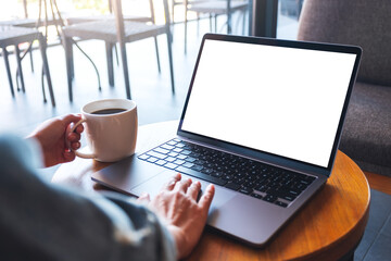 Mockup image of a hand touching on laptop computer touchpad with blank white desktop screen while drinking coffee
