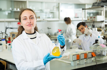 Young female lab technician working with reagents in test tubes during chemical experiment..
