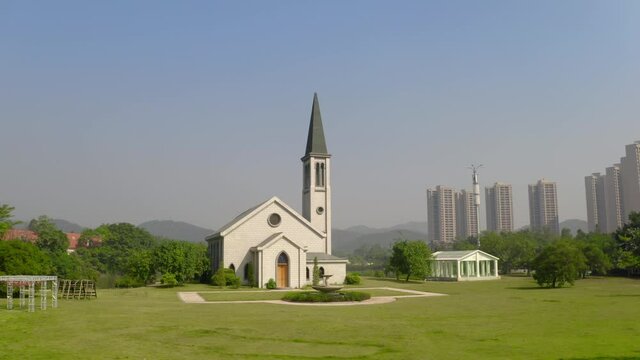 Catholic style church building without a cross surrounded with green grass fields on a bright clear day. Aerial  pivot shot.