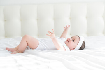 Obraz na płótnie Canvas Cute healthy baby girl 6 months smiling in a white bodysuit lying on a bed on white bedding.