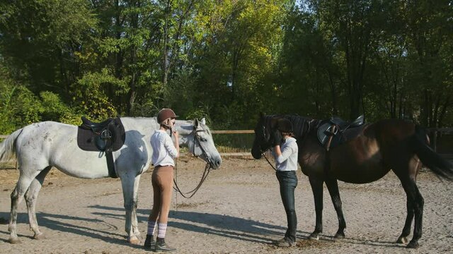 Two Female riders in riding clothes and helmets prepare to ride on their horses