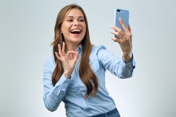 Smiling woman using smartphone for video chat and doing OK gesture.
