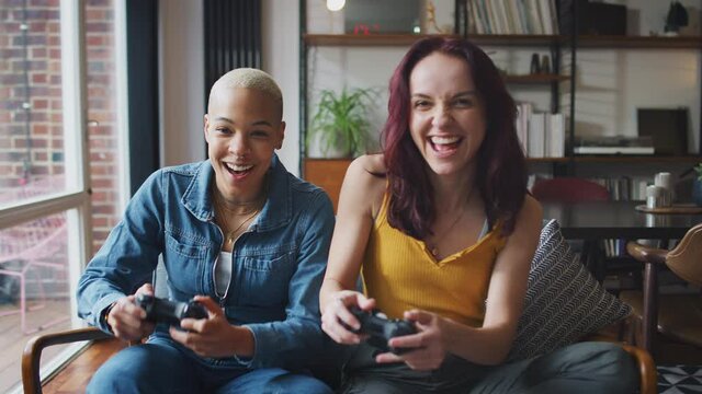 Same sex female couple sitting on sofa at home playing computer game together - shot in slow motion