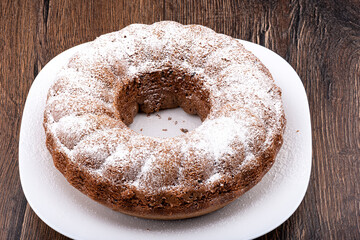 A ring-shaped cupcake sprinkled with powdered sugar. Homemade cupcake on a white plate over a wooden background.