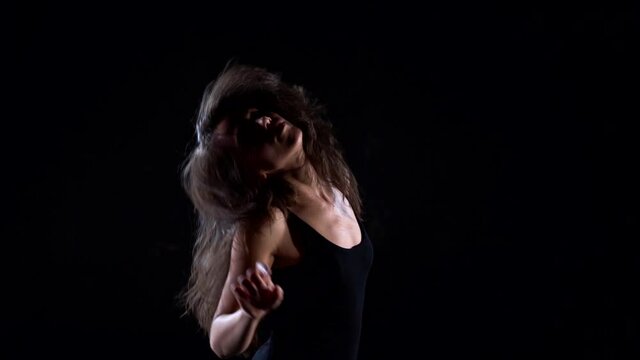 young energetic, plastic woman in a black suit in the Studio on a dark background dancing, moving and posing.