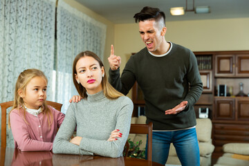 Annoyed man and woman quarreling in presence of their little daughter at home