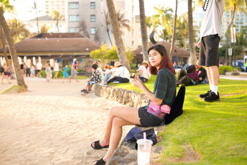 Teen female sitting along Waikiki beach eating at sunset