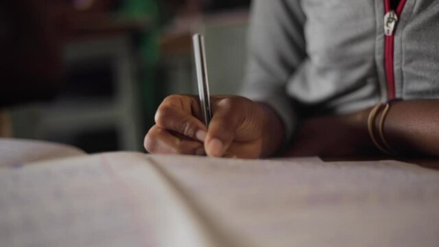 Close up shot African young kids children school students is writing with pencil doing homework in education class behind desk in village learning for the future job Tanzania 25 fps slowmotion