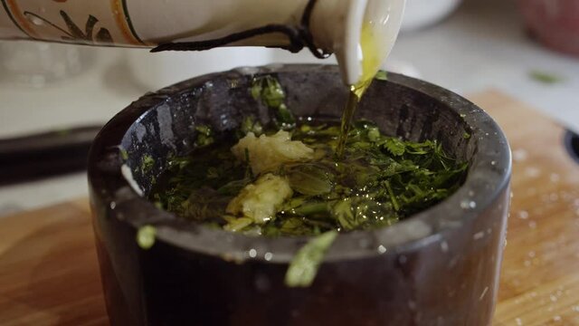 Adding olive oil into a bowl with garlic and herbs. Close up.  Organic sauce making