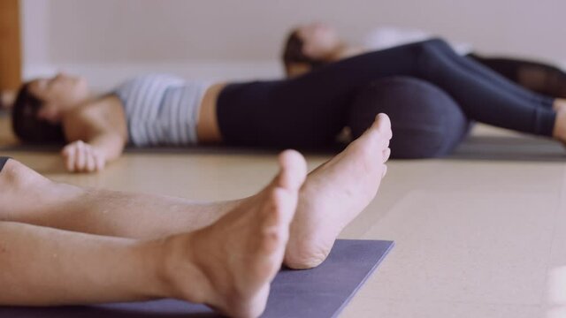 Yoga class does shavasana pose in studio, camera raises to reveal participants