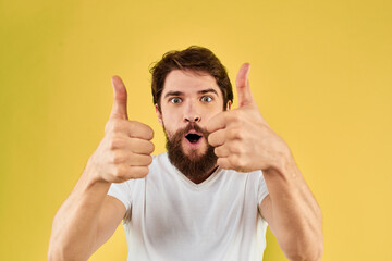 Bearded man emotions fun gesture with hands white t-shirt close-up yellow background