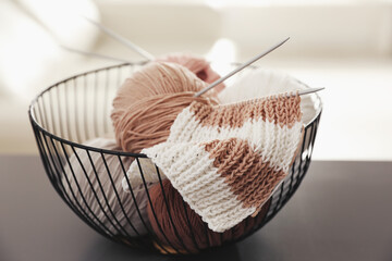 Yarn balls and knitting needles in metal basket on grey table against blurred background. Creative...