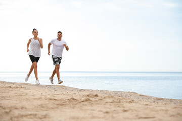 Couple running together on beach, space for text. Body training