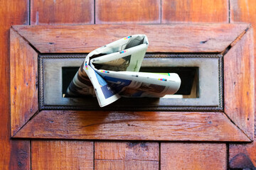 newspaper, paper, tabloid, journal stuffed through mail slot of mailbox, postbox on a wooden street door