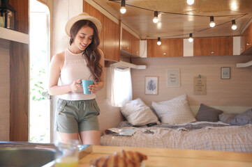 Young woman with cup in trailer, space for text. Camping vacation