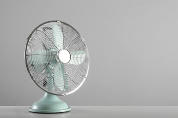 Electric fan on table against light grey background, space for text. Summer heat