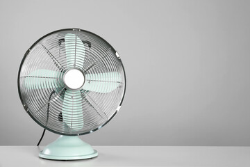 Electric fan on table against light grey background, space for text. Summer heat