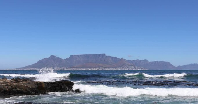 Beautiful clear day looking from Robben Island to table mountain and mother city with ocean waves crashing over rocky shore line on Robben Island

