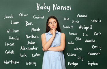 Thoughtful pregnant woman choosing name for her child. Future mother near green chalkboard with different names