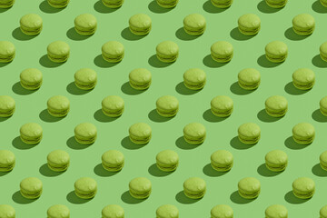 Green macaroons with shadows on colored background. Trendy minimal seamless pattern. French cookies...