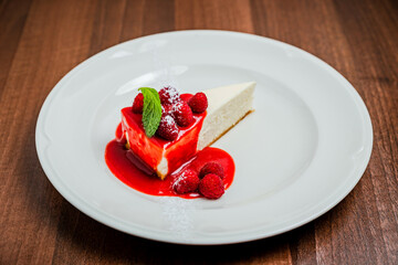 A piece of classic cheesecake new york, raspberry syrup topping, garnished with fresh berries and mint, white plate