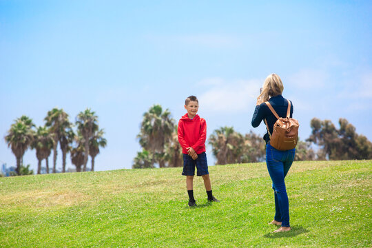A Mother taking a cell phone photo of her posing and smiling son at an outdoor park in California on a sunny day