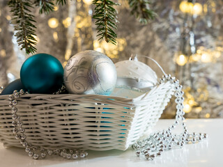 Basket with colorful balls, a branch of a Christmas tree on a silvery blurred background with...