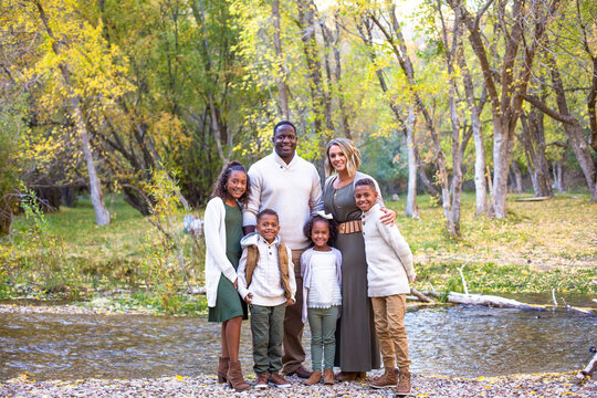 Cute mixed race family portrait outdoors. standing together in nature with the fall colors in the background. A full length posed photo of Smiling, happy, diverse multi ethnic family