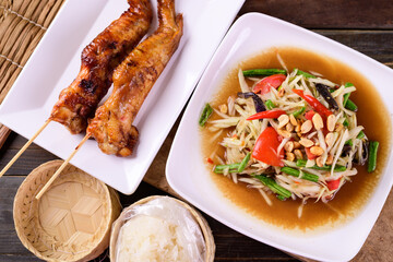 Thai food (Som Tum), Spicy green papaya salad eating with grilled chicken wing and sticky rice on wooden background, Top view