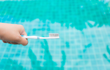 Old toothbrush in girl hand over blurred blue pool water background, reuse brush for cleaning, outdoor day light