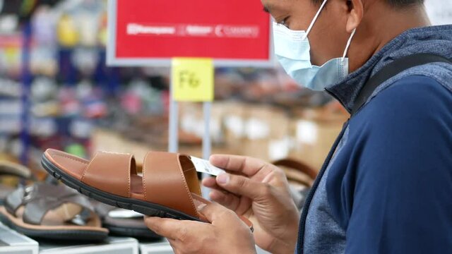 A handsome Indonesian young man is choosing sandal at a shop