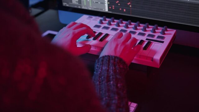 Recording music notes, playing electronic keyboard, midi keys in music sequencer. Hands and midi controller on the table with neon lights, man composing music in night