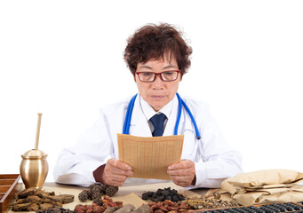 The old Chinese doctor in a white coat in the pharmacy is carefully looking at the prescription