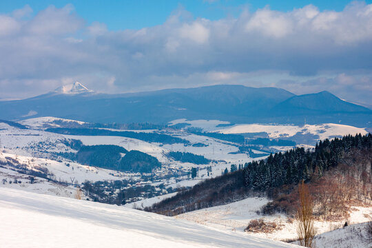 rural landscape in wintertime. trees on the snow covered hill. beautiful scenery of carpathian mountains. village in the distant valley. wonderful frosty and sunny weather, clouds on the sky
