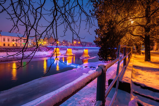 uzhhorod, ukraine - 26 DEC, 2016: old town on a christmas night. beautiful cityscape by the river. snow on the embankment. bridge and lanterns glowing in the distance