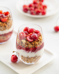 Granola Parfait with Yogurt, oat granola, fresh cherry, jam and honey in tall glass. Healthy dessert. Low depth of field, selective focus.