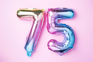 Rainbow foil balloon number, digit seventy-five. Birthday greeting card with inscription 75. Anniversary concept. Top view. Colored numeral on pink background. Numerical digit, Celebration event