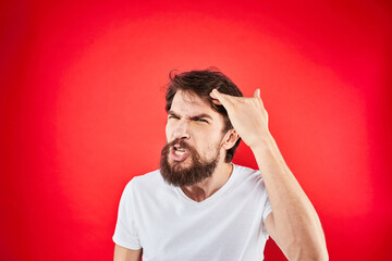 Emotional bearded man gestures with his hands in a white T-shirt aggression discontent red background