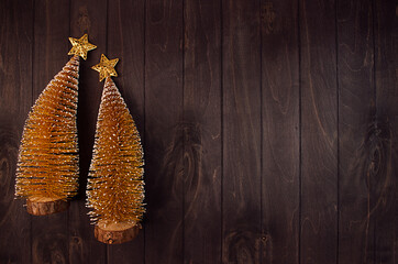 Elegant christmas decoration - two festive golden glittering trees and glossy stars on dark brown wood board, top view, copy space, New Year background.