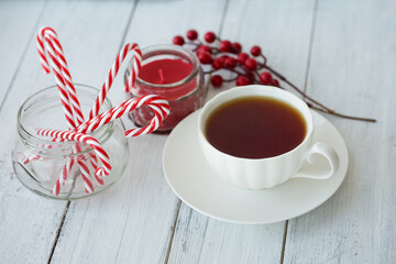 Tea, candle, Christmas canes and berries on a white wooden background.